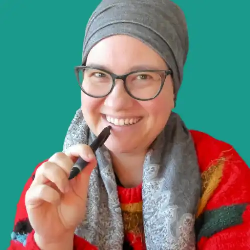 Smiling photo of Anna Crosby wearing glasses, a gray headscarf, and a red sweater, holding a stylus pen against a teal background.